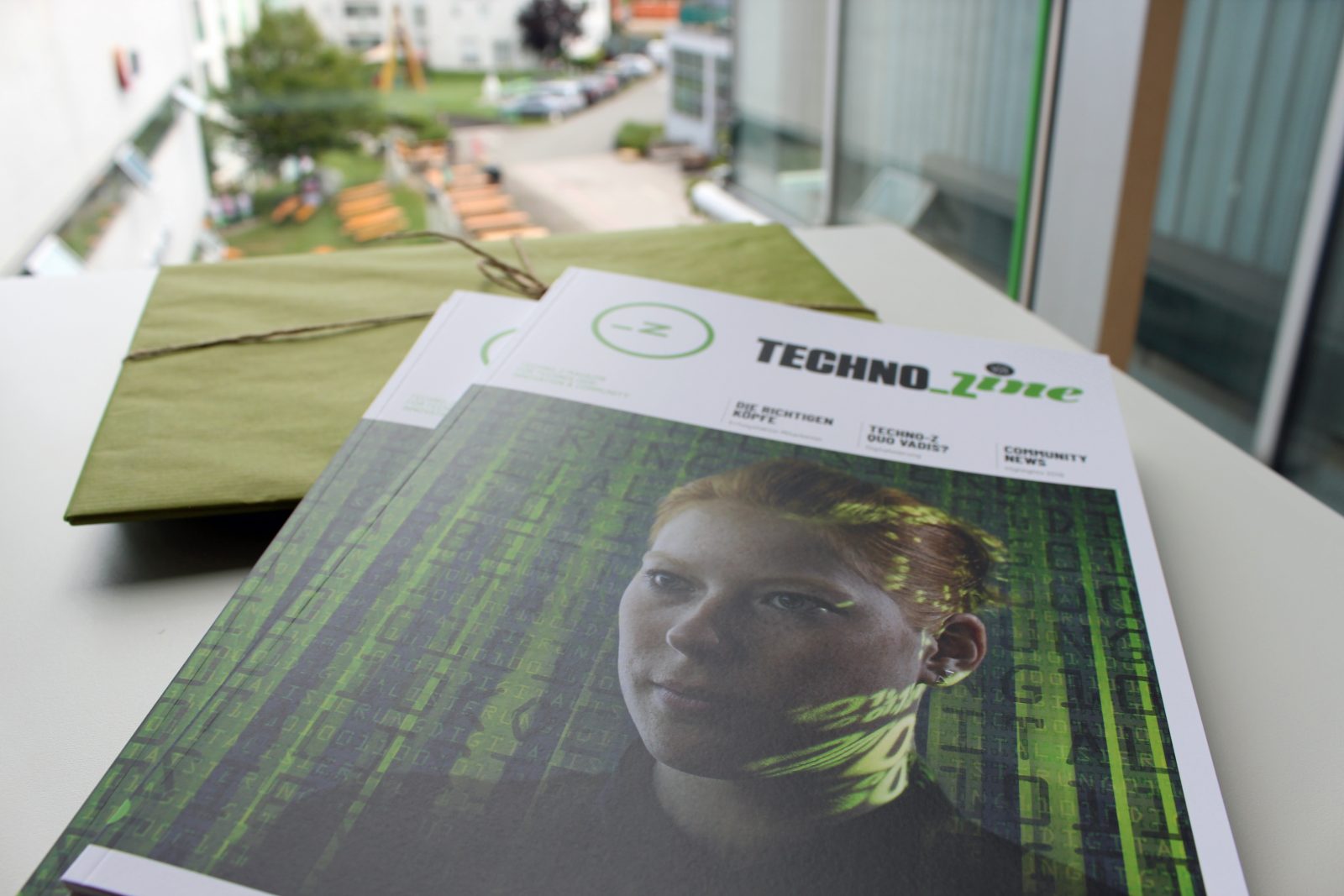 Das Print-Magazin des Techno-Z liegt auf einem Tisch. Im Hintergrund das Fenster mit Aussicht auf die grüne Wiese des Techno-Z