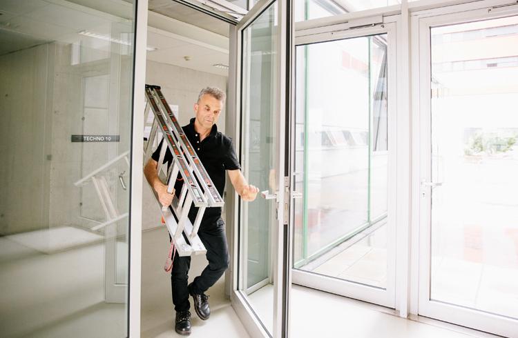Hannes Niederreiter geht mit Leiter auf der Schulter durch eine Glastür im Techno-Z Salzburg.