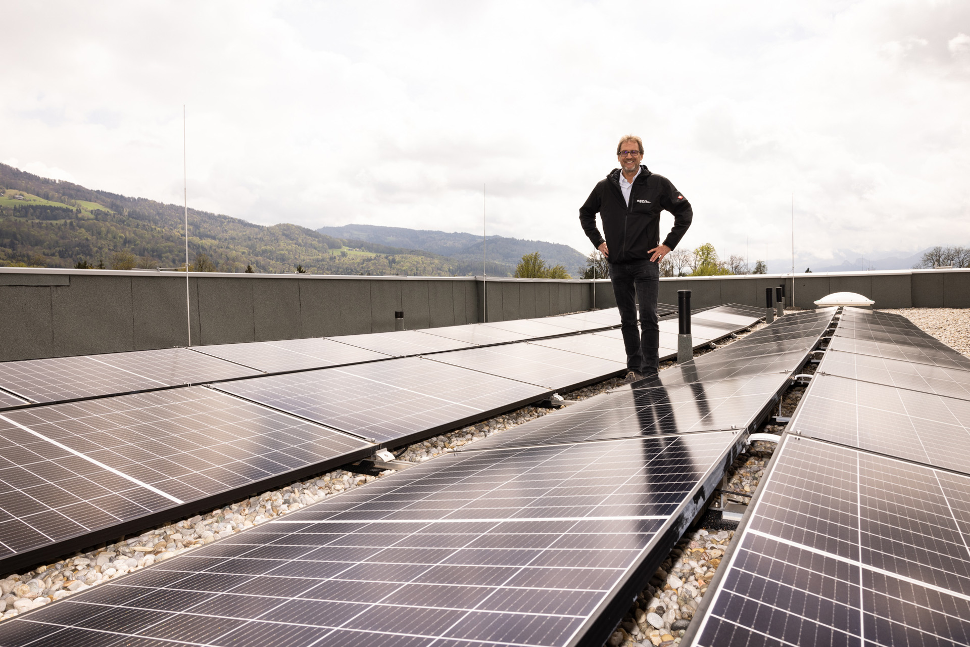 Dietmar Stampfer steht auf einem geschotterten Flachdach umgeben von Photovoltaik-Panelen.